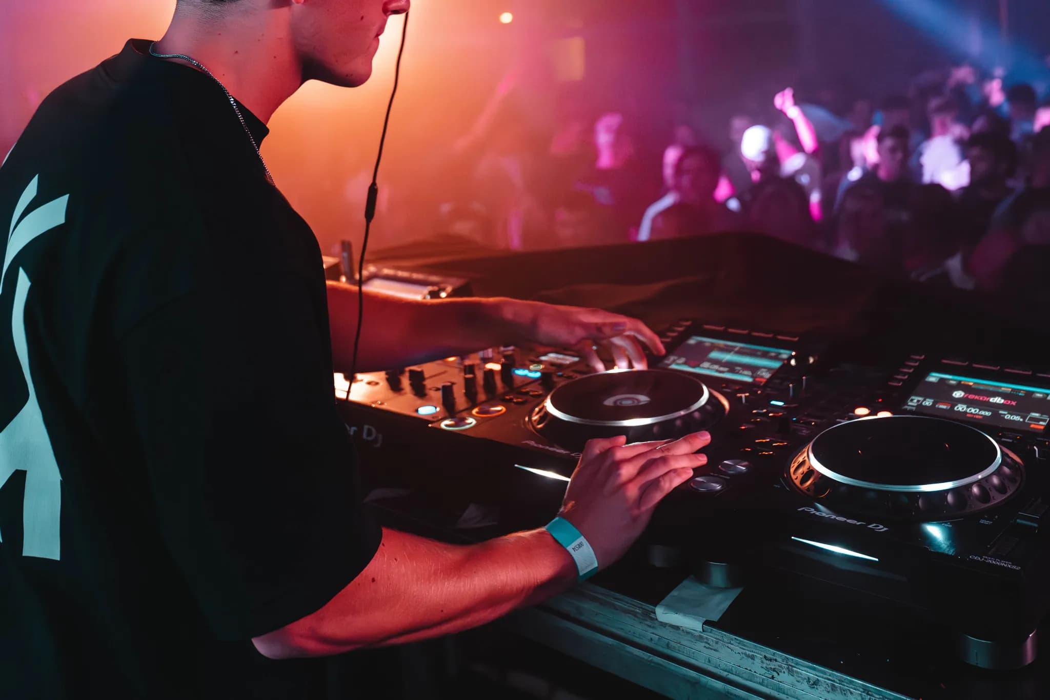 DJ met koptelefoon achter de draaitafels op een festival, met gekleurd licht en publiek